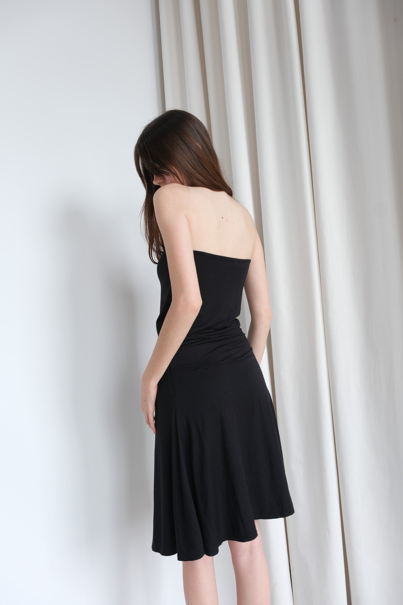 Woman wearing a black strapless dress against a white curtain background