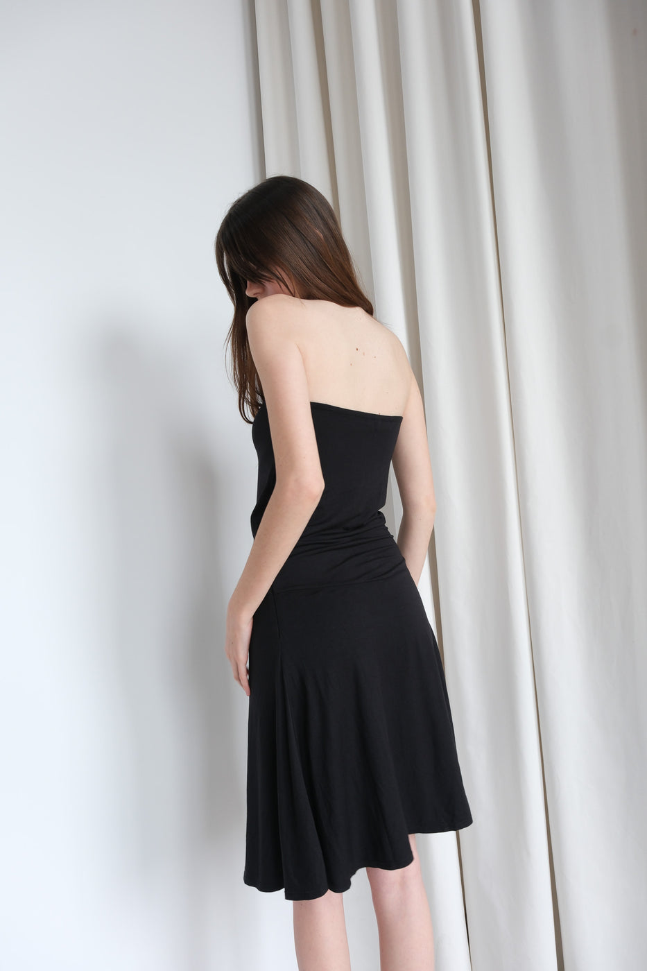 Woman wearing a black strapless dress against a white curtain background