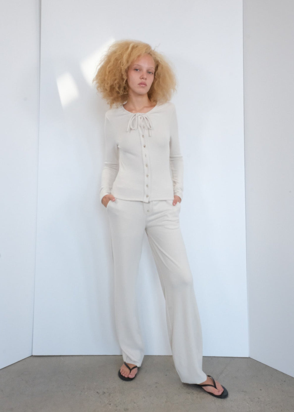 Woman wearing a white outfit standing against a plain white wall.