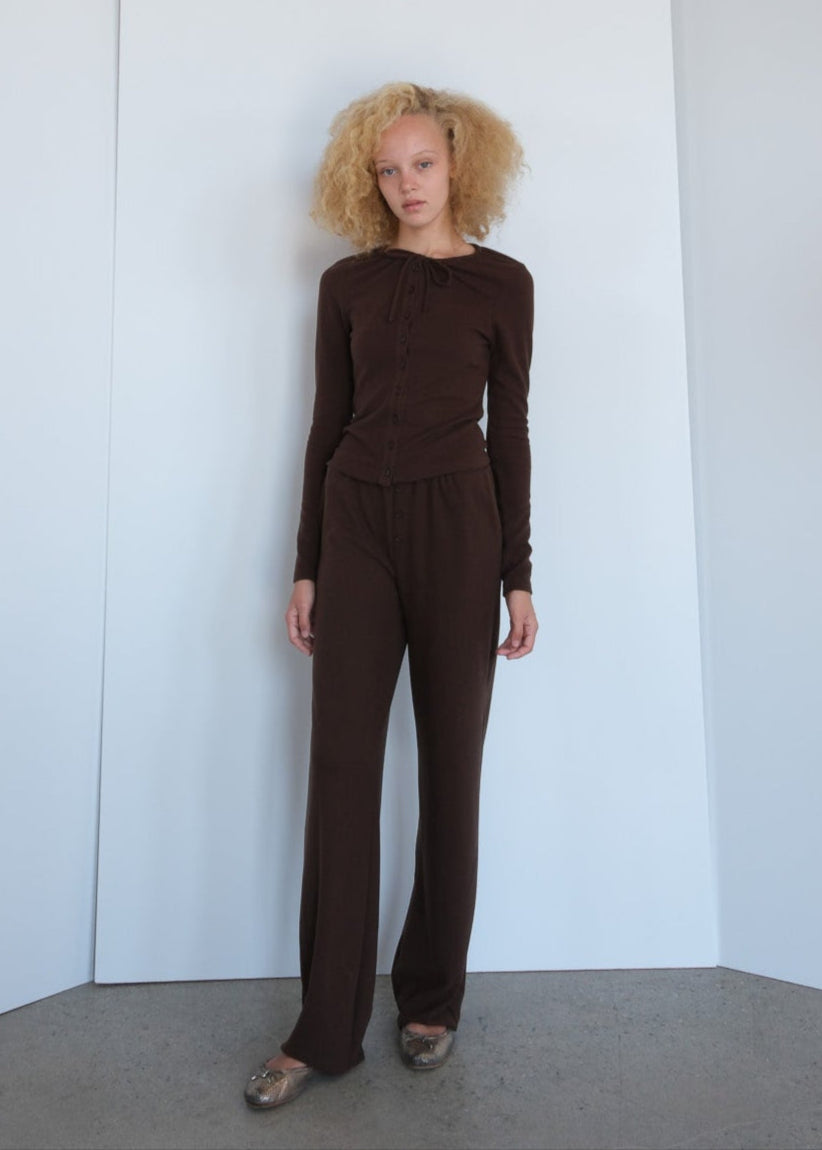 Person wearing a brown outfit standing against a white wall.